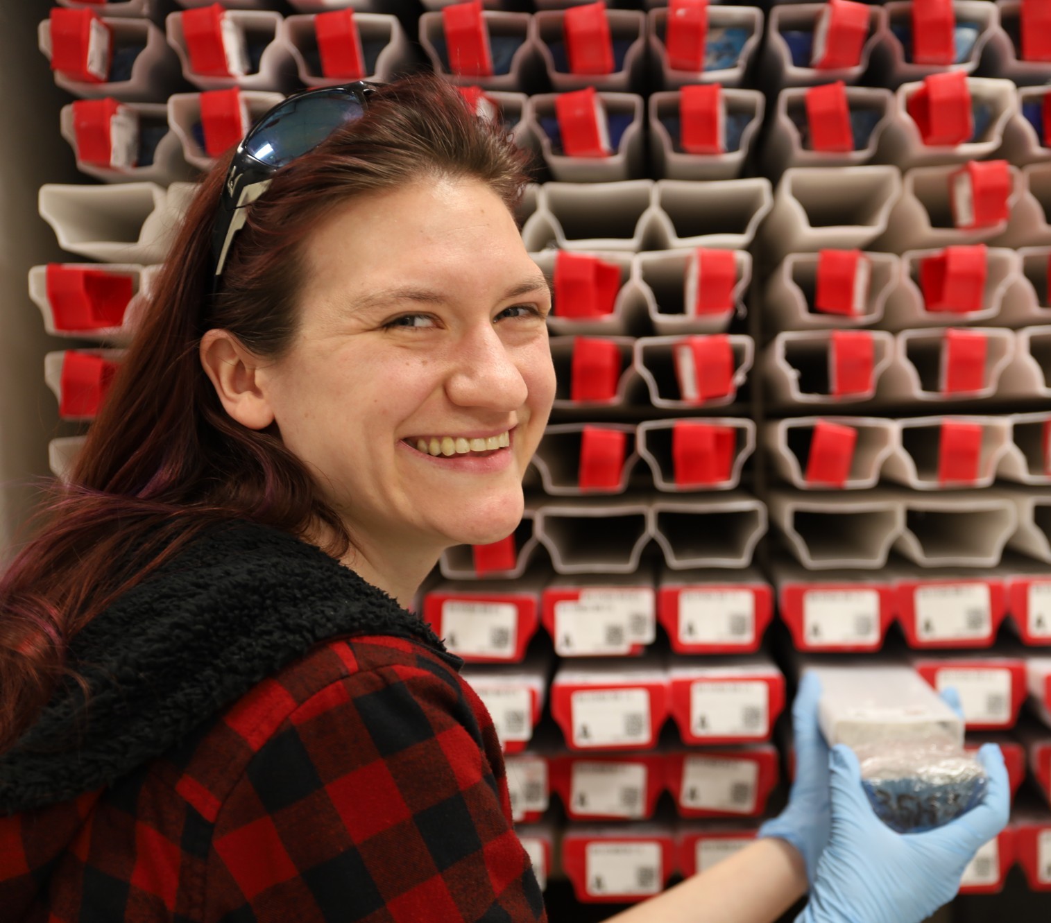 Jennifer Middleton standing in front of a rack of sediment cores from IODP Expedition 383